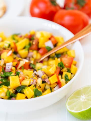 A white bowl with mango salsa and a gold spoon in the bowl.