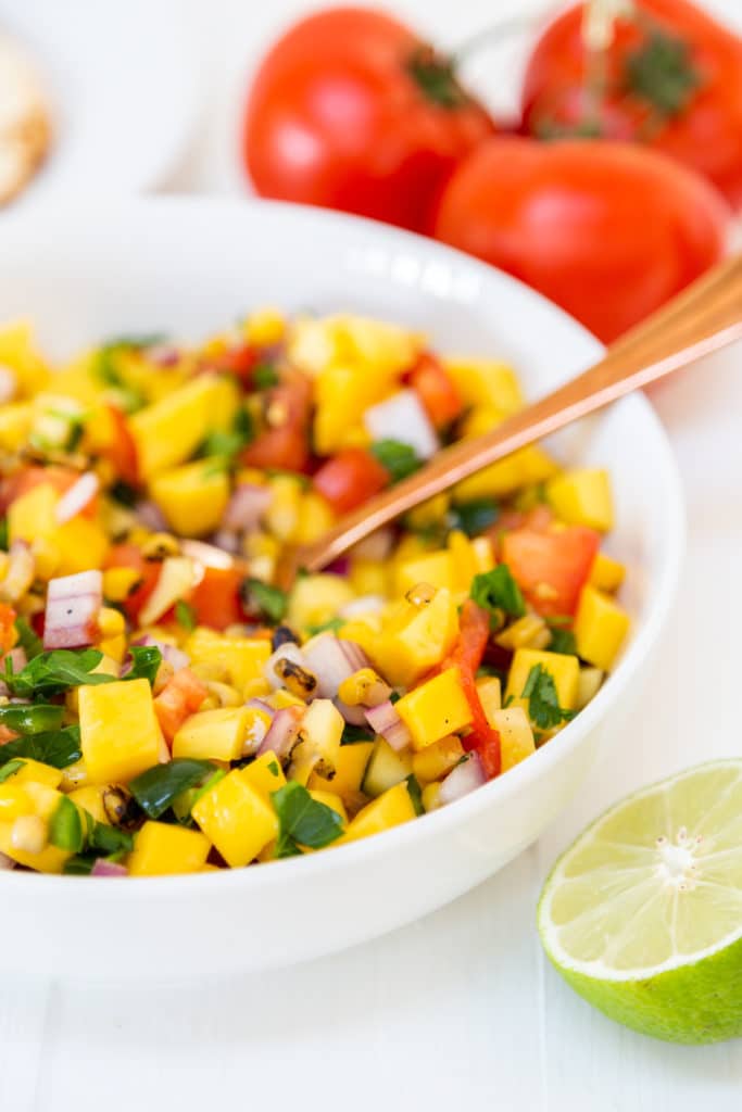 A white bowl with mango salsa and a gold spoon in the bowl.