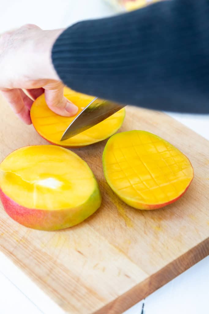 A woman dicing a mango with a chef's knife.