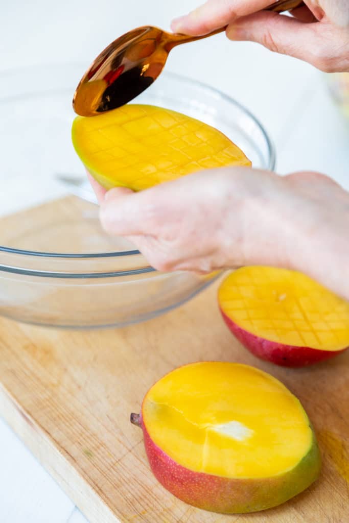 A hand holding a gold spoon that's scooping out diced mango from the fruit.