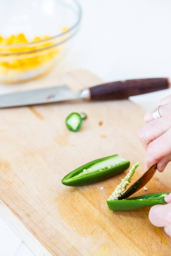 A jalapeno pepper cut in half with a hand removing the core with a spoon.