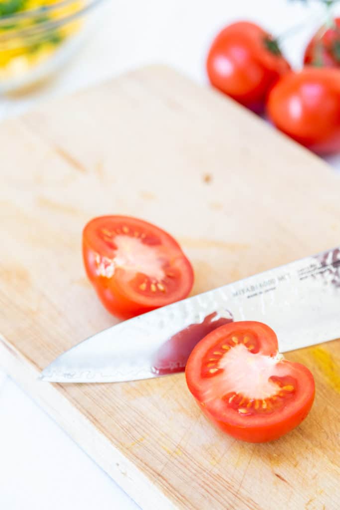 A chef's knife cutting a red tomato in half. 