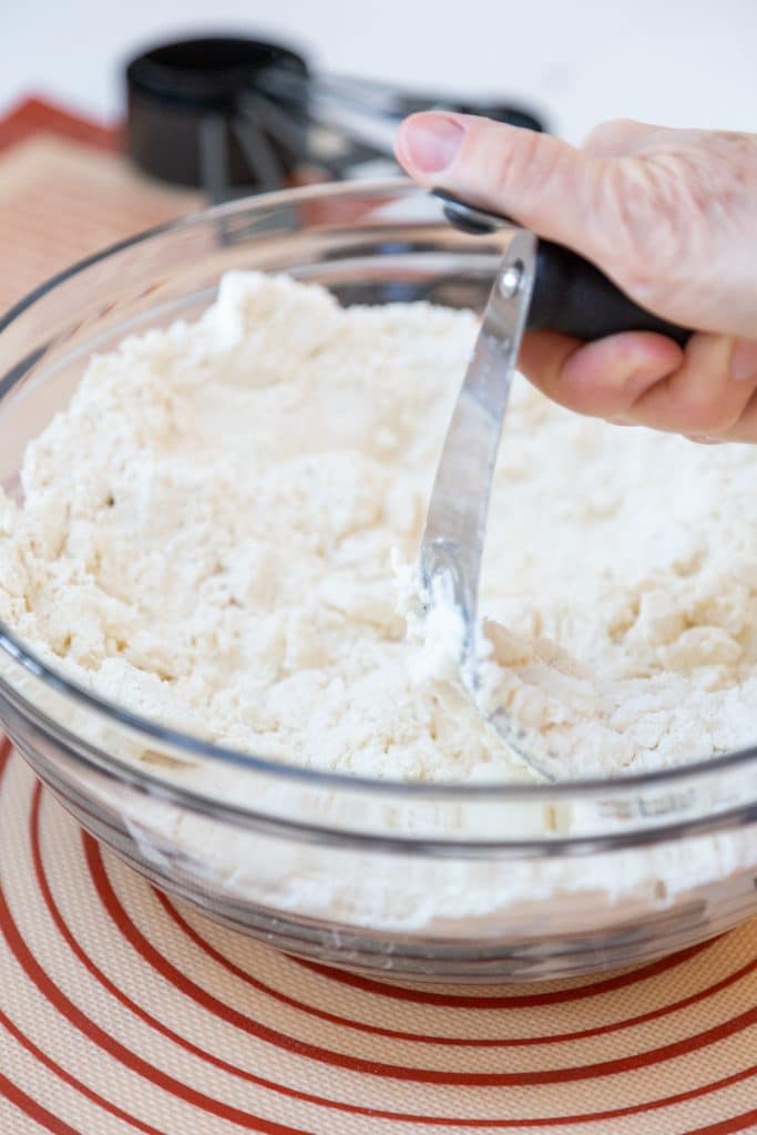 A hand pressing a pastry cutter into a bowl of flour and butter.