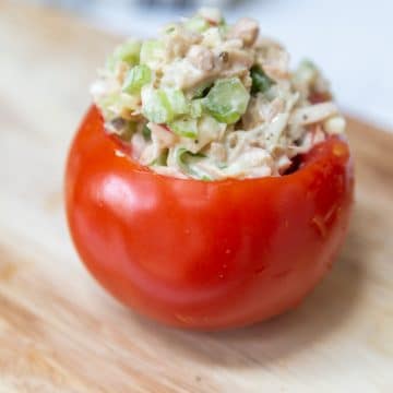 A red tomato stuffed with chicken salad on a wooden board.