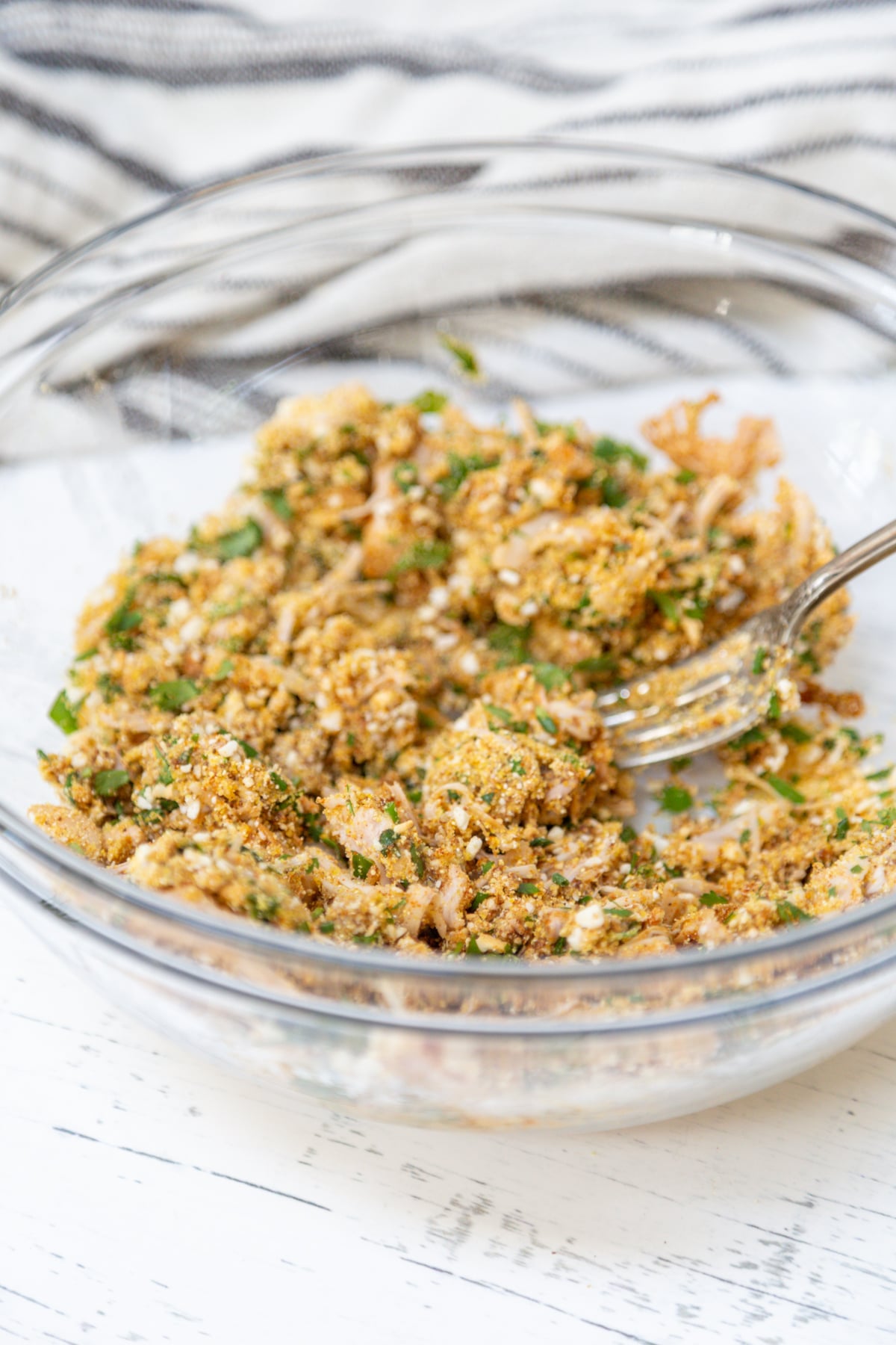 A clear glass bowl with uncooked crab cake mixture.