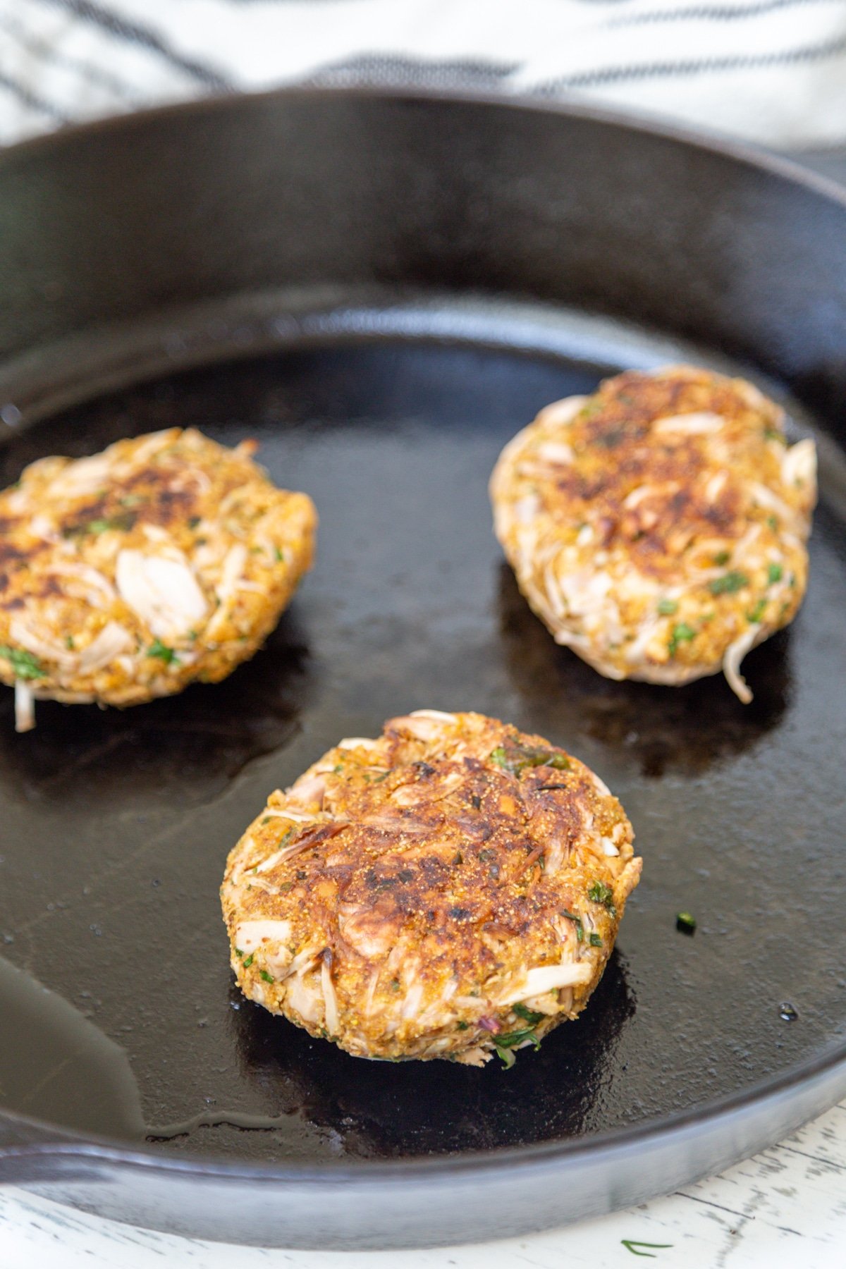 3 fried crab cakes in a cast iron pan.
