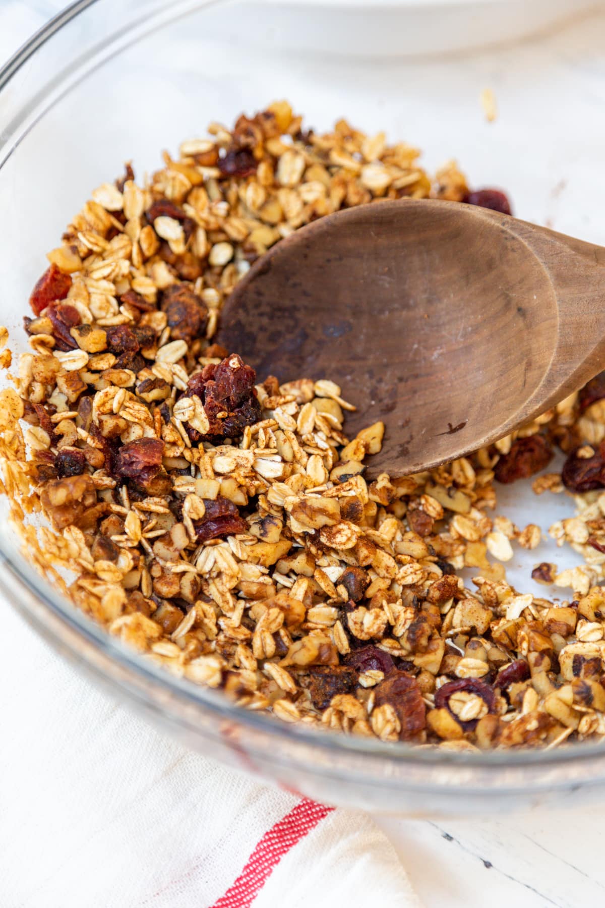 A glass mixing bowl with oat and dried fruit filling for baked apples with a wooden spoon.