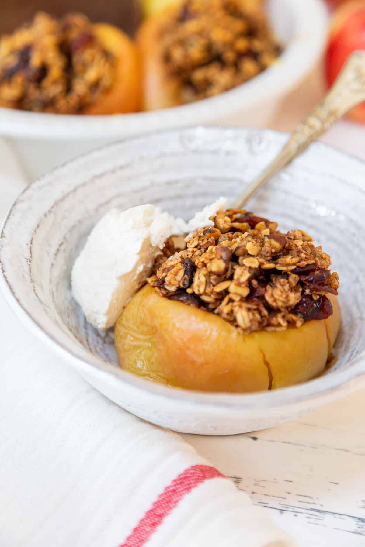 A baked apple stuffed with an oat filling and a scoop of vanilla ice cream on the side in a white bowl. 