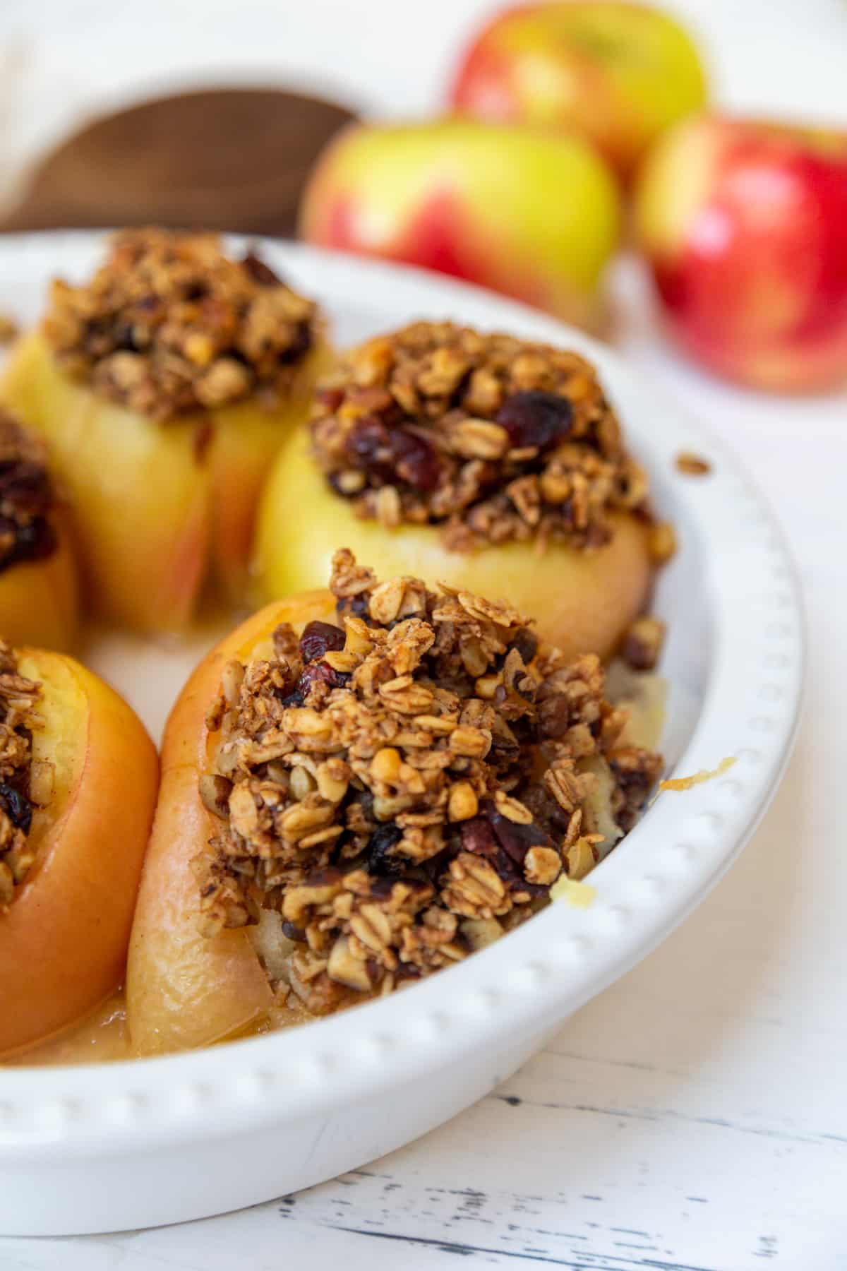 A white round baking dish with stuffed baked apples and raw apples in the background.