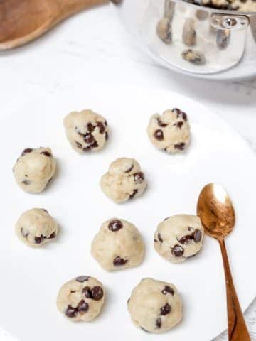 Chocolate chip cookie dough balls on parchment paper with a brass spoon.
