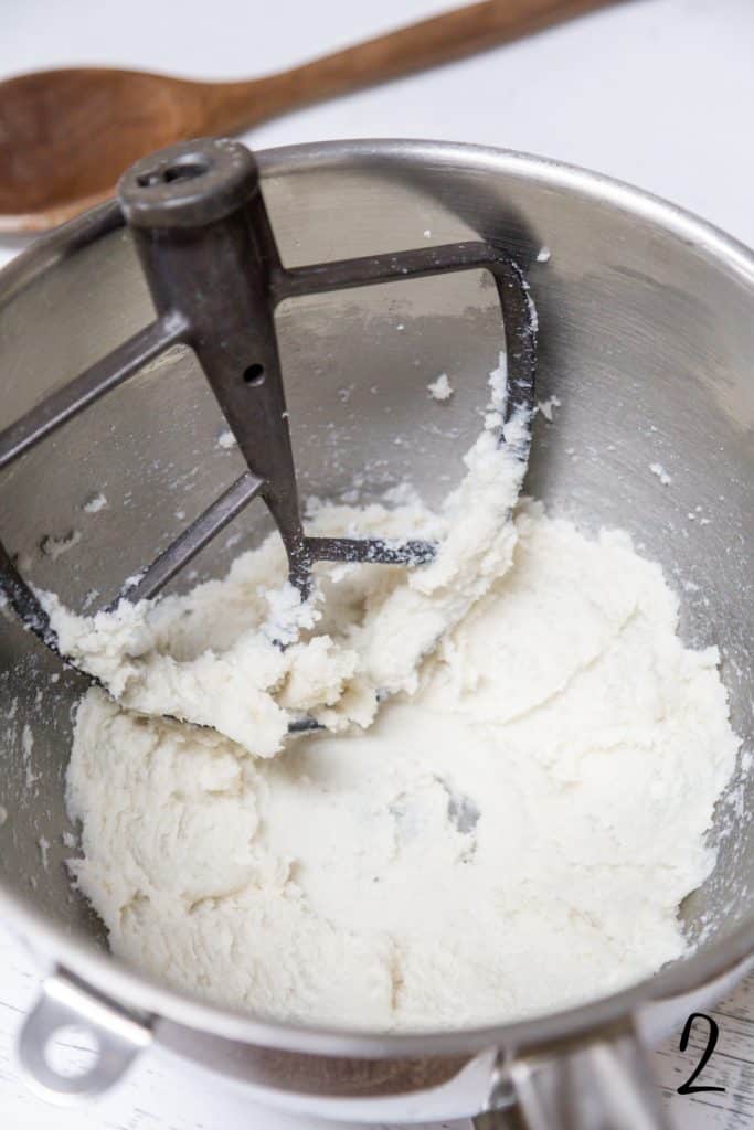 Whipped butter and sugar in a large silver mixing bowl with a paddle attachment.