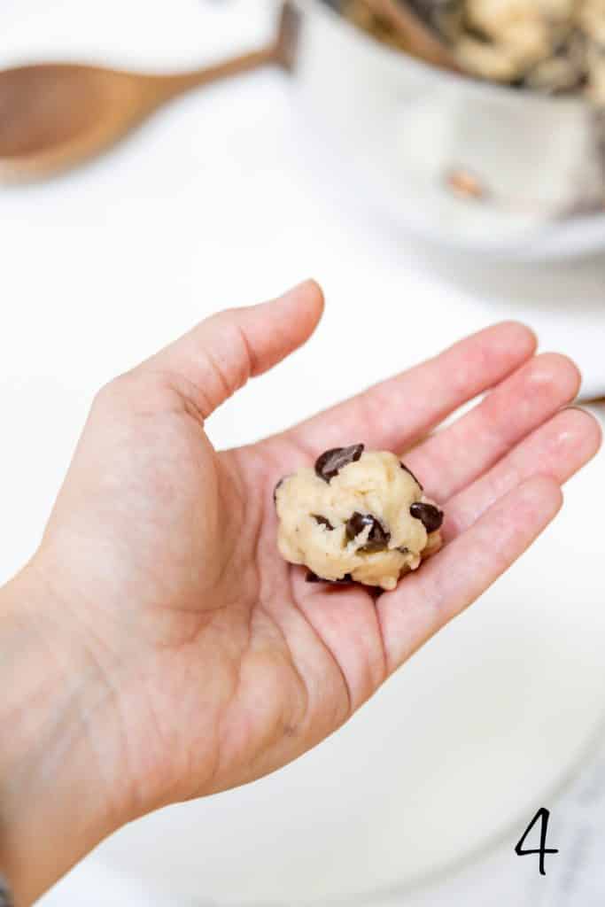 A hand holding a chocolate chip cookie dough ball.