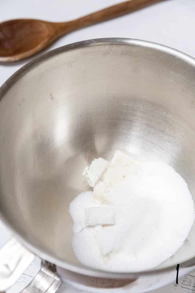 A silver mixing bowl with white sugar inside of it.