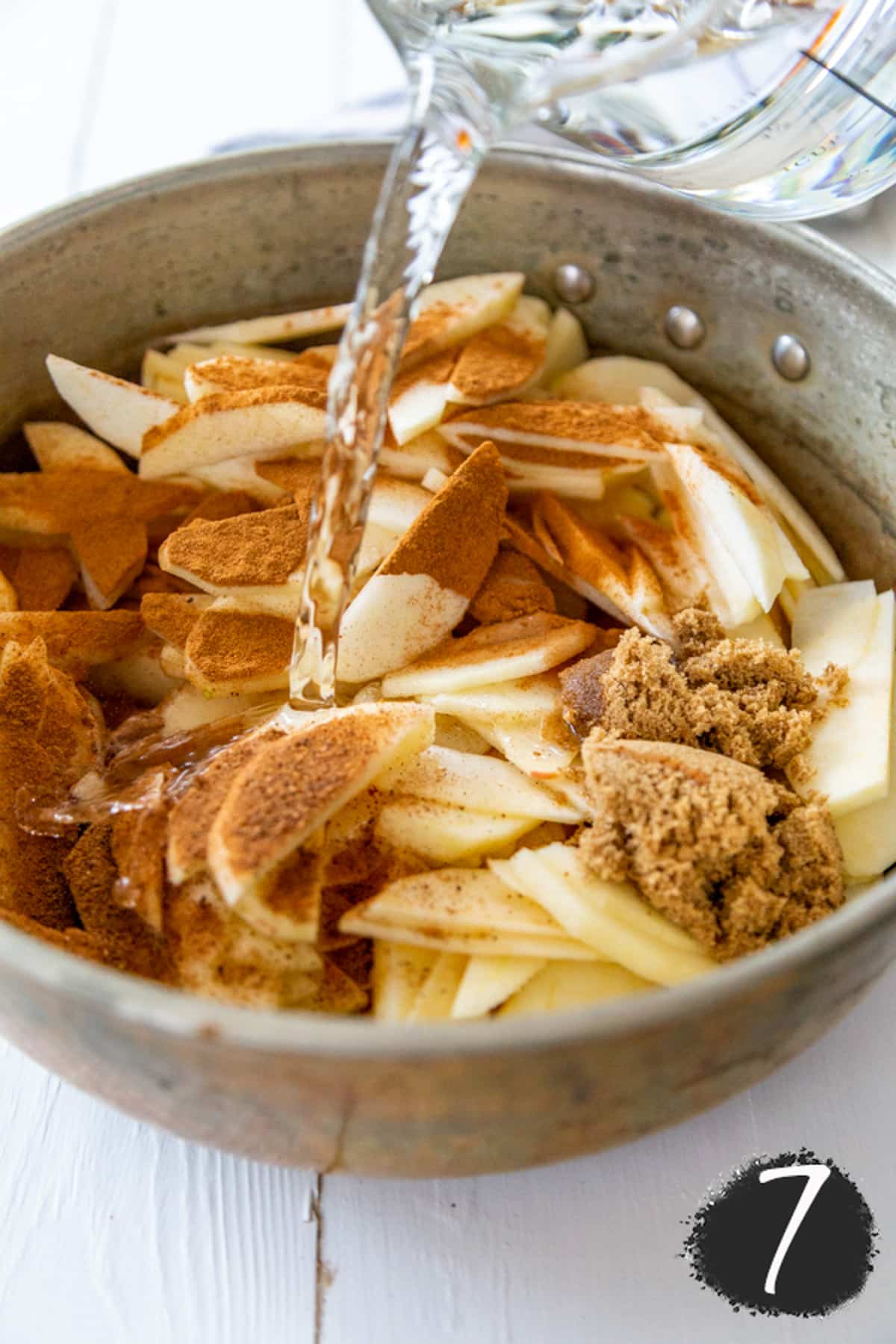 Water being poured into a copper pot filled with sliced apples and spices.