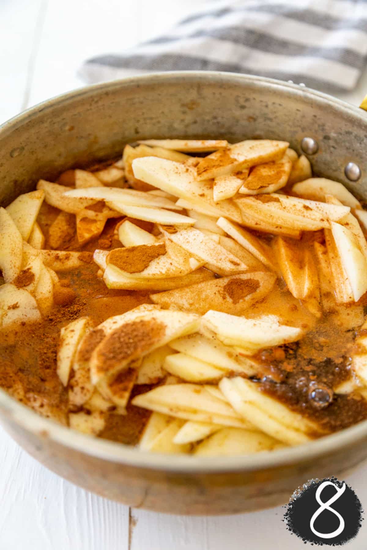 A copper pot with sliced apples, water, and spices.