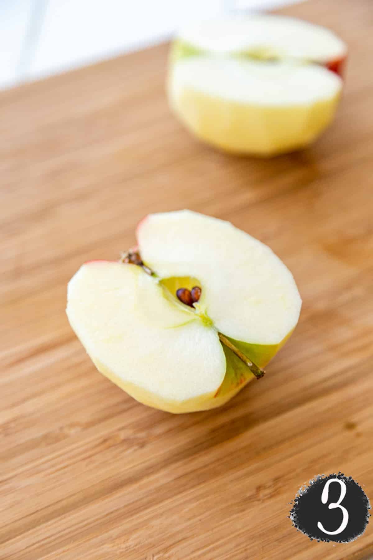 A peeled apple cut in half on a wooden board.