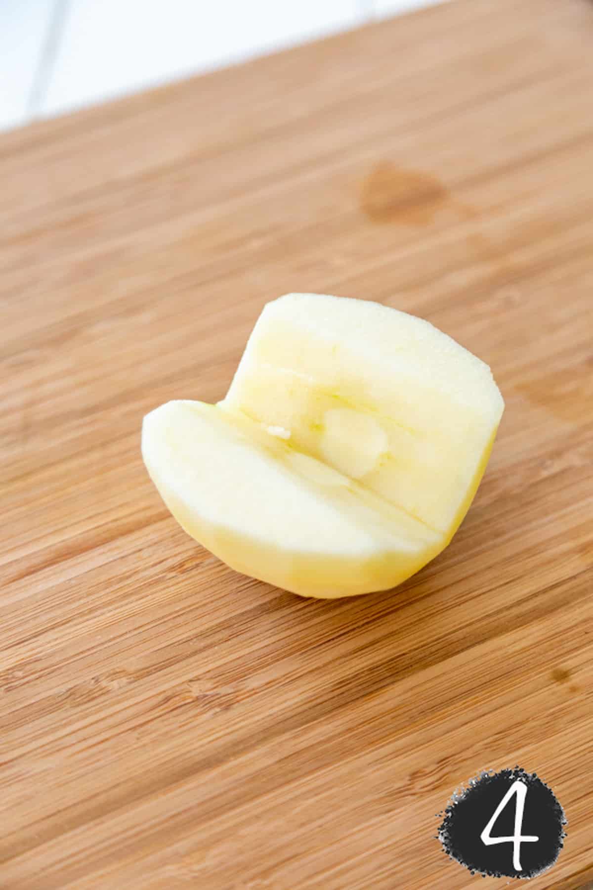 Half of a peeled and cored apple on a wooden board.