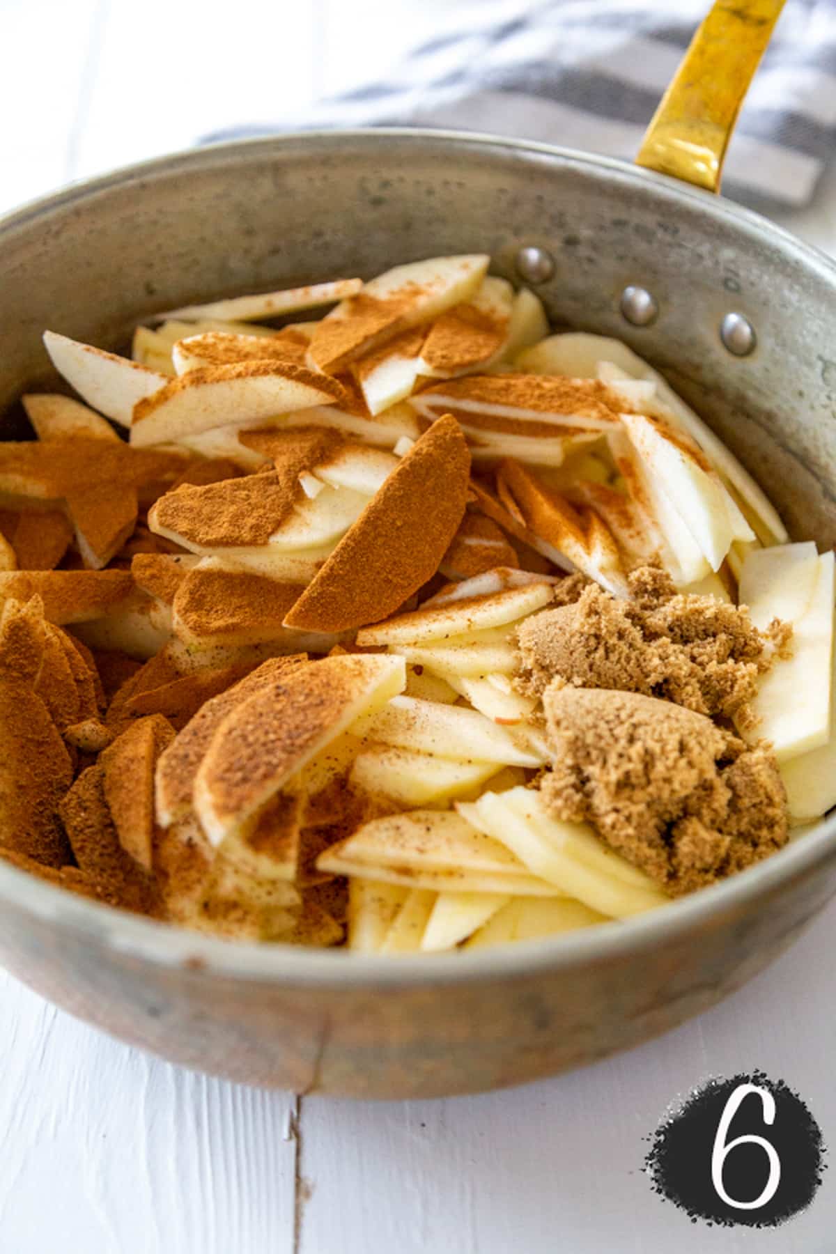 A copper pot with sliced apples and spices.