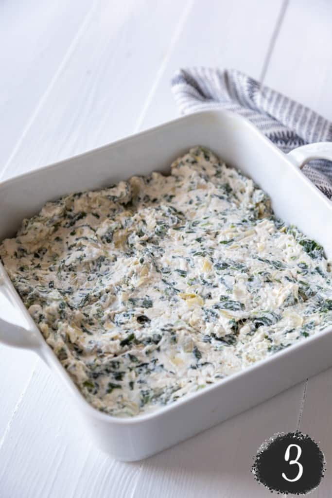 Unbaked vegan spinach artichoke dip in a square white baking dish.