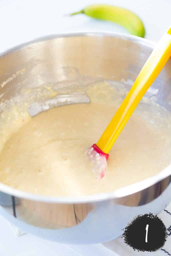 A silver mixing bowl with a yellow and red spatula stirring yellow cake batter.
