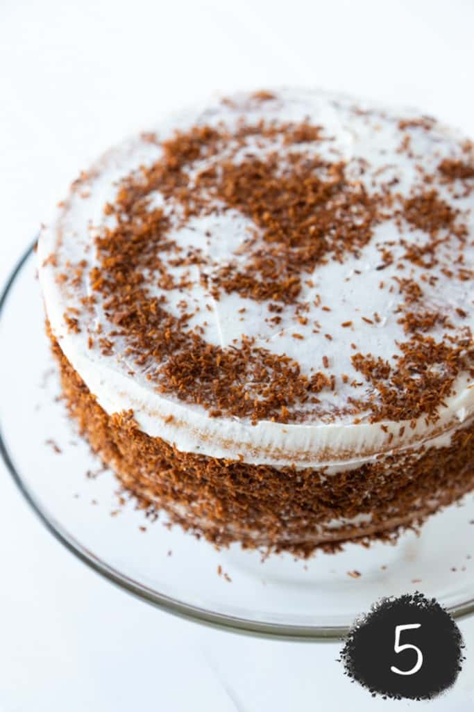 A 2 layer cake with white frosting and toasted coconut sprinkled over it.