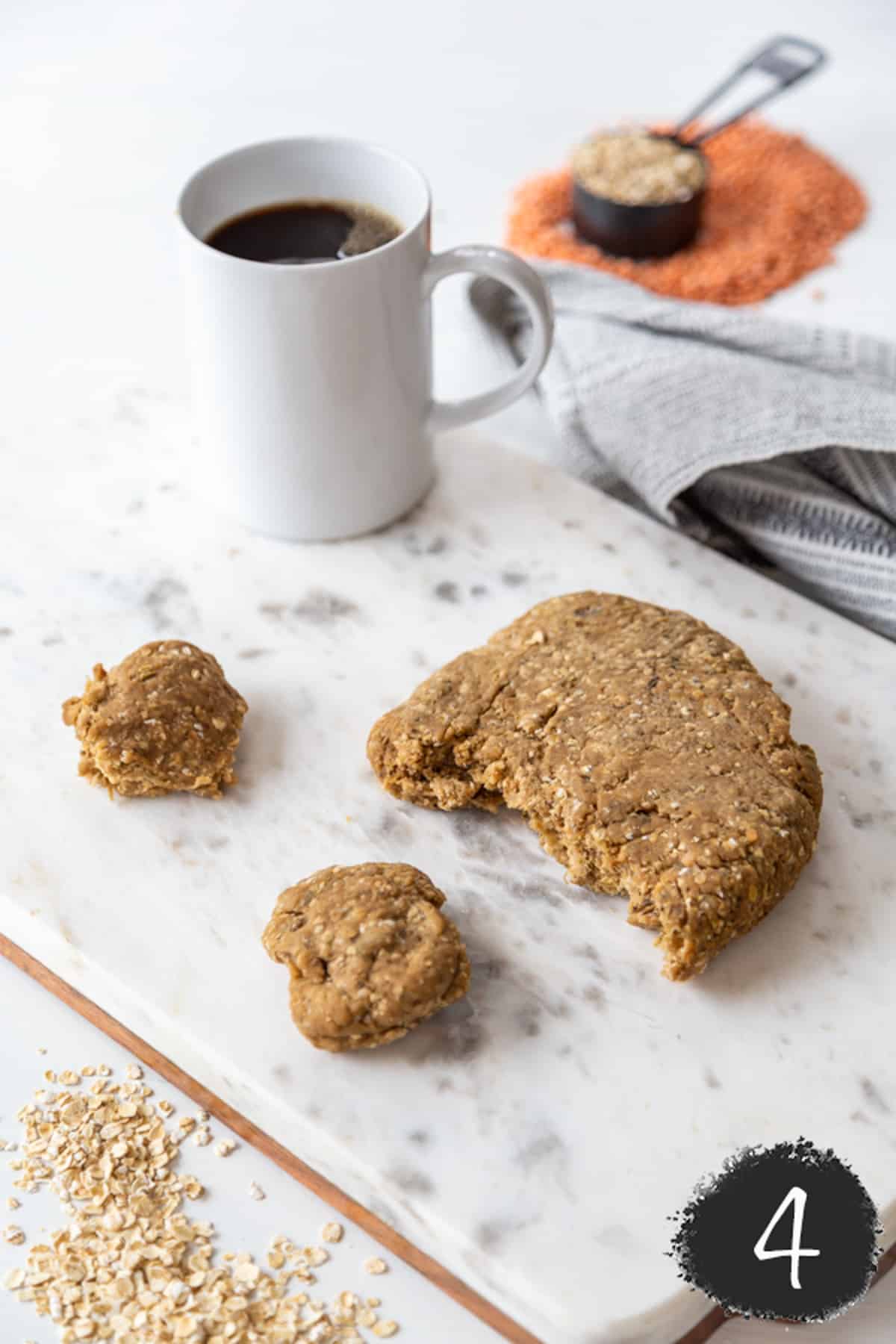 Sausage dough on a marble board with pieces torn off of it and a white mug of coffee.