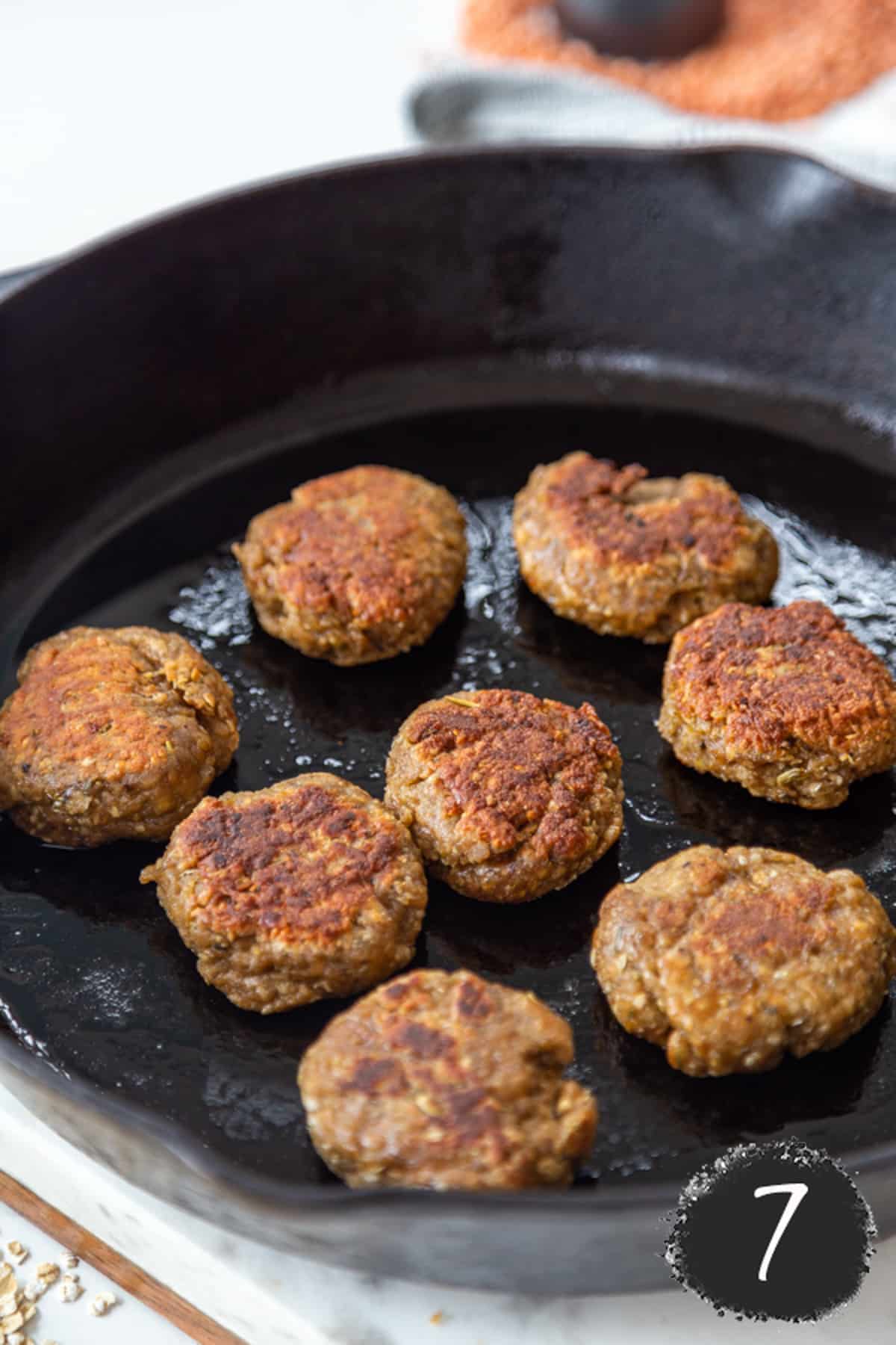 Vegan breakfast sausage patties frying in an iron skillet.