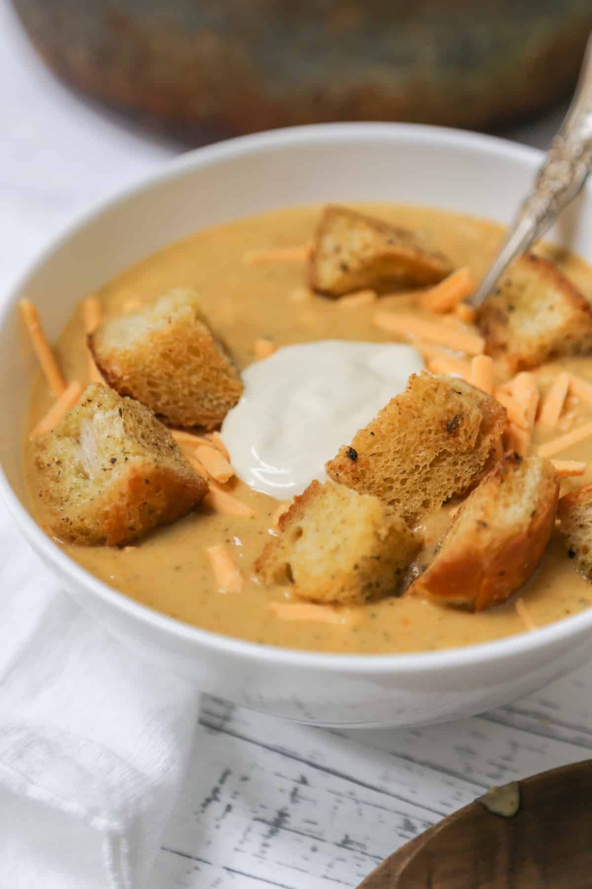 A bowl of cheddar broccoli soup with croutons, sour cream and shredded cheese.