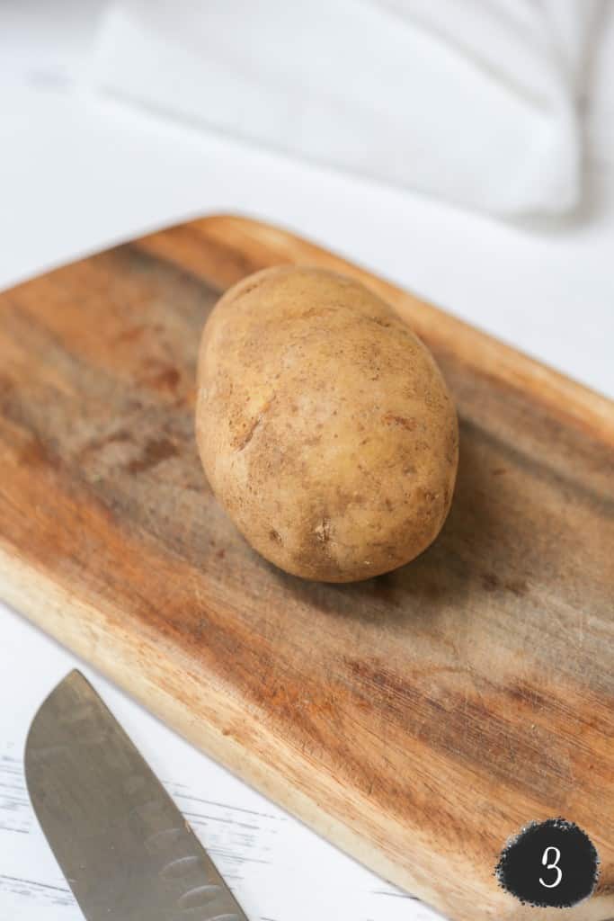 A potato on a cutting board with a knife next to it. 