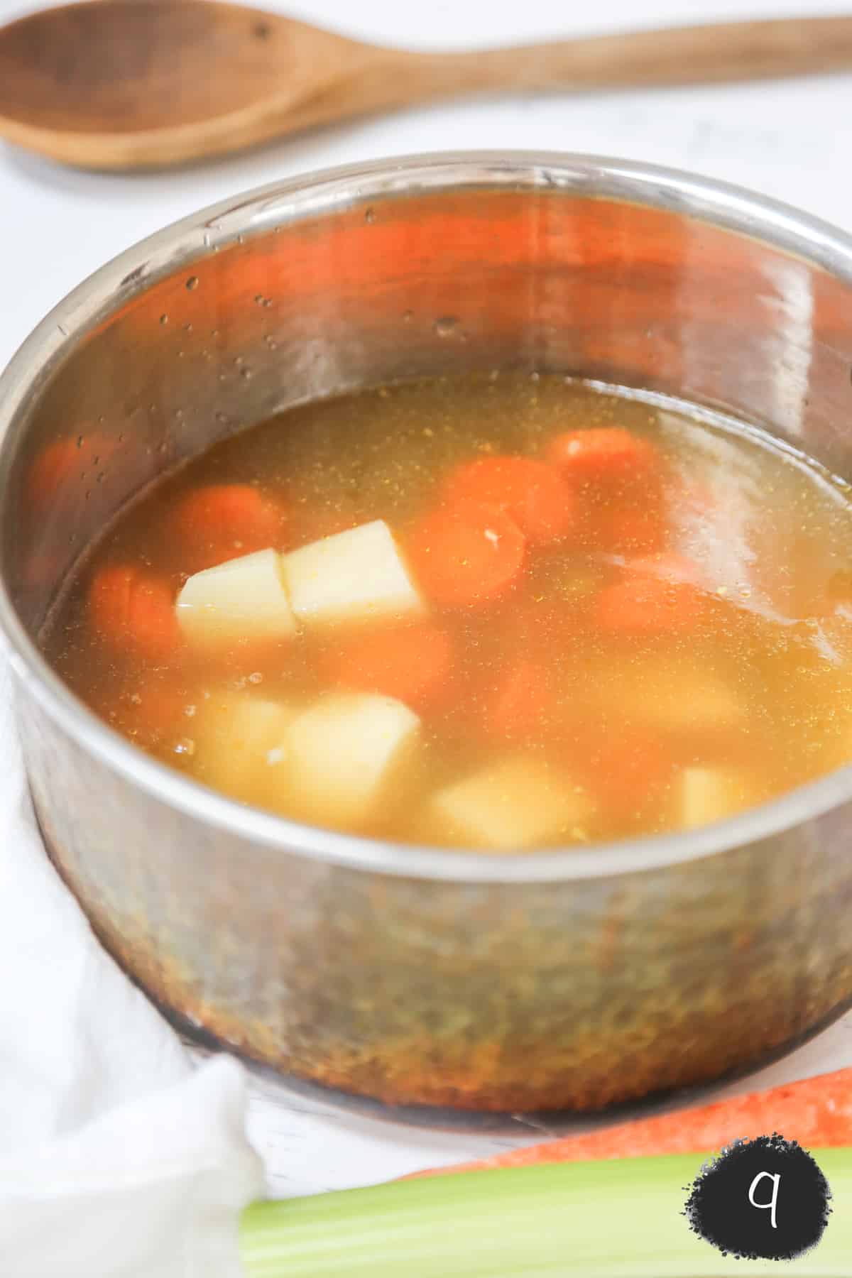 A copper pot with broth, potatoes, and carrots.