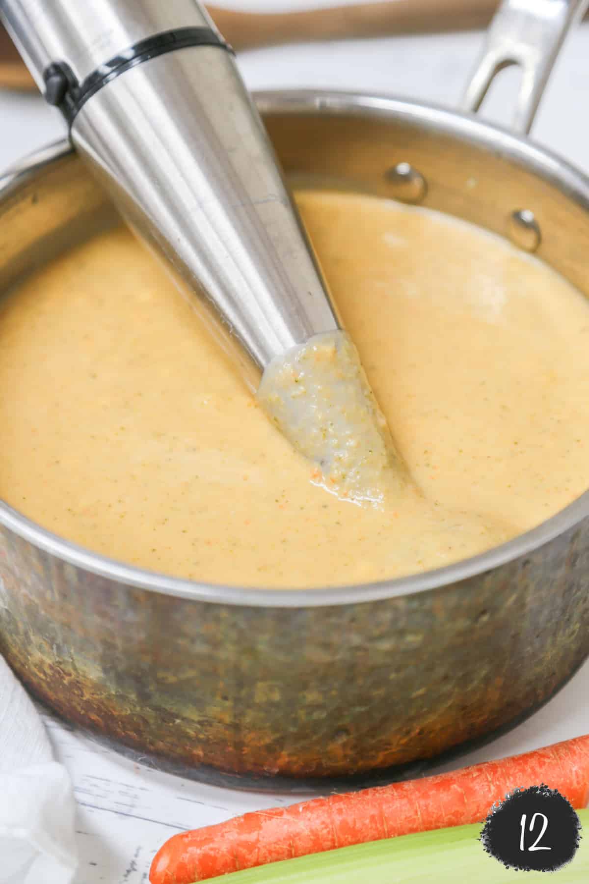An immersion blender in a pot of creamy broccoli soup.