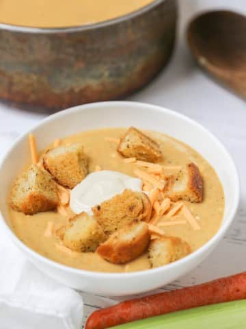 A white bowl with broccoli soup and croutons with the pot of soup behind it.