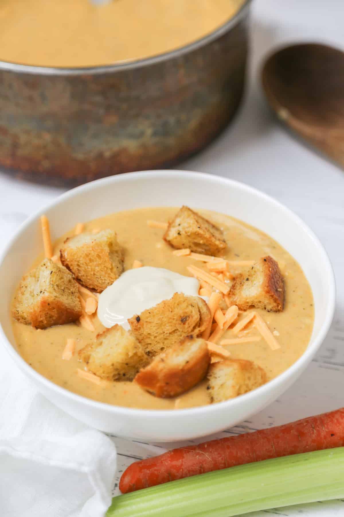 A white bowl with broccoli soup and croutons with the pot of soup behind it.