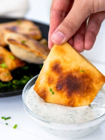 A hand dipping a mini calzone into a bowl of ranch dressing.