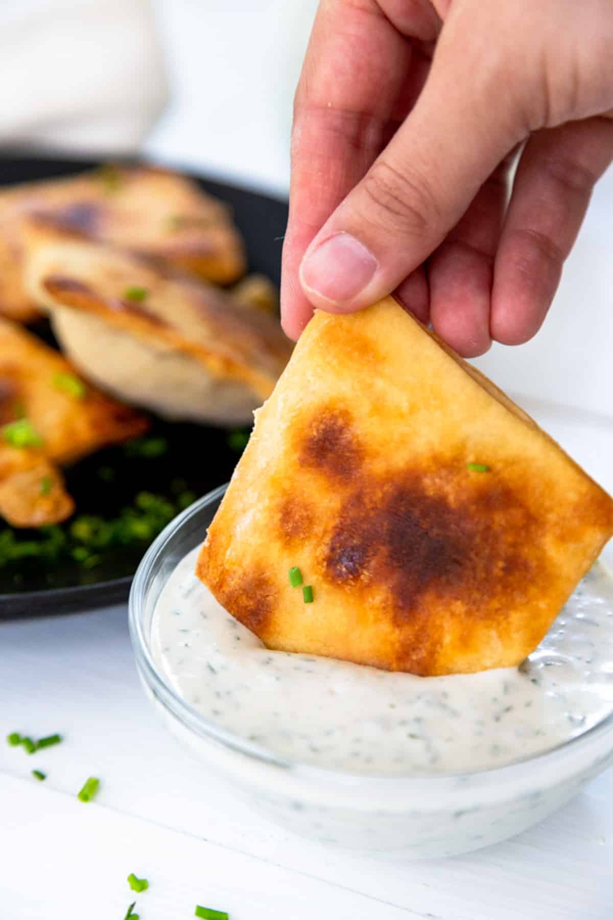 A hand dipping a mini calzone into a bowl of ranch dressing.