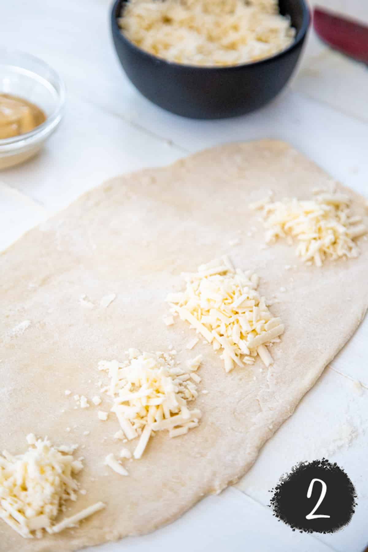 Pizza dough rolled into a long strip with Dollops of shredded white cheese.