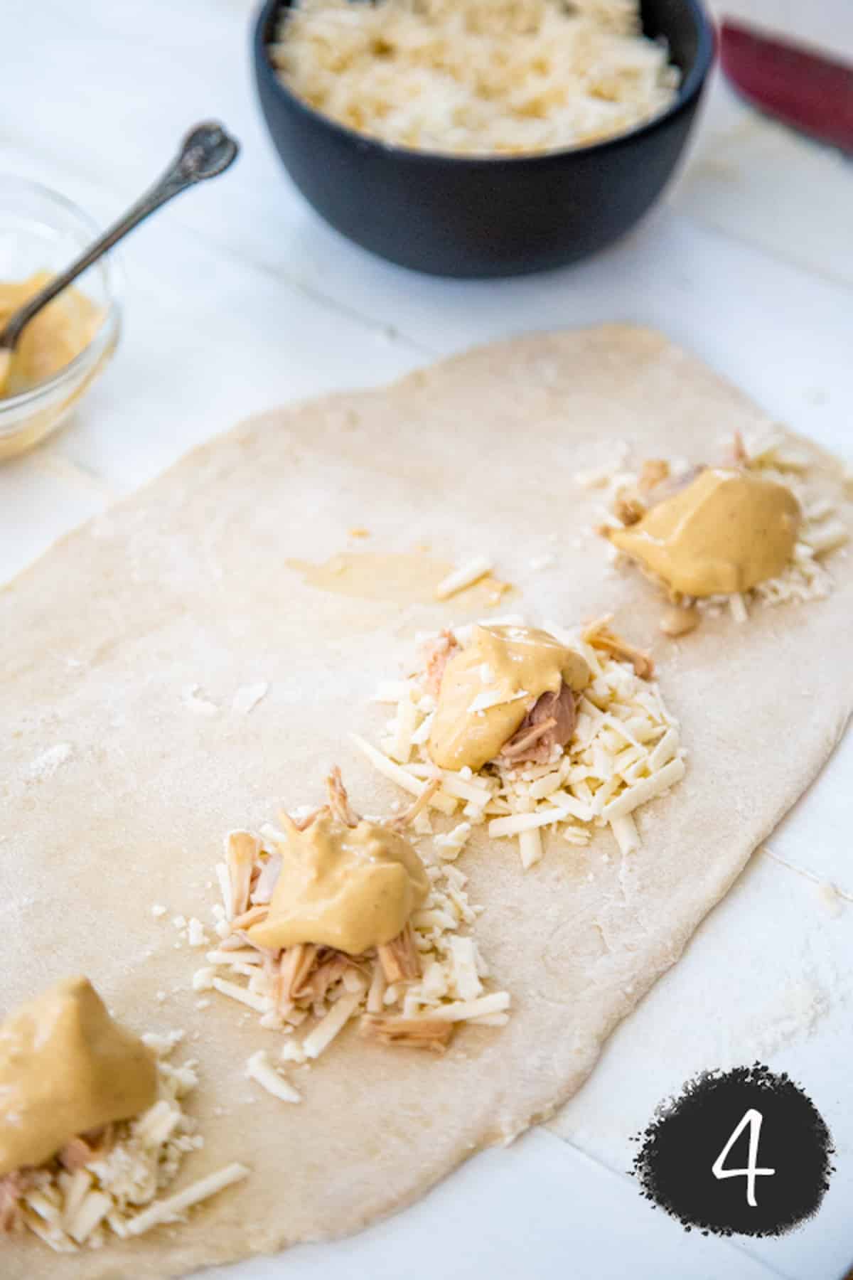 Pizza dough with dollops of cheese, shredded jackfruit, and sauce.