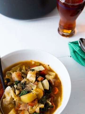 A white bowl of cabbage soup with a glass of beer.