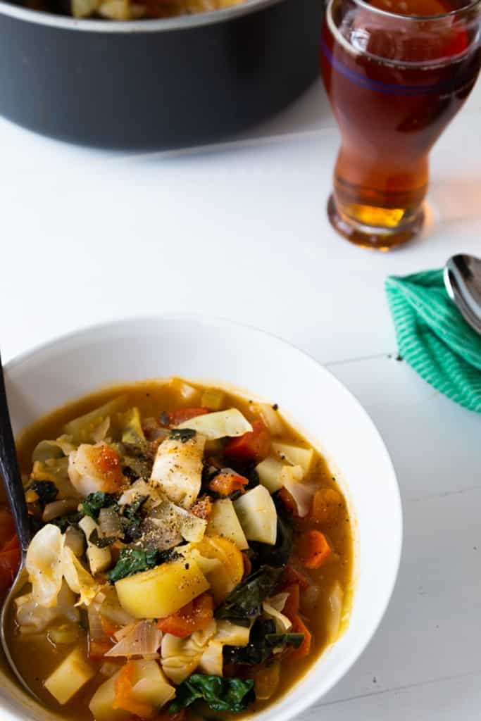 A white bowl of cabbage soup with a glass of beer.