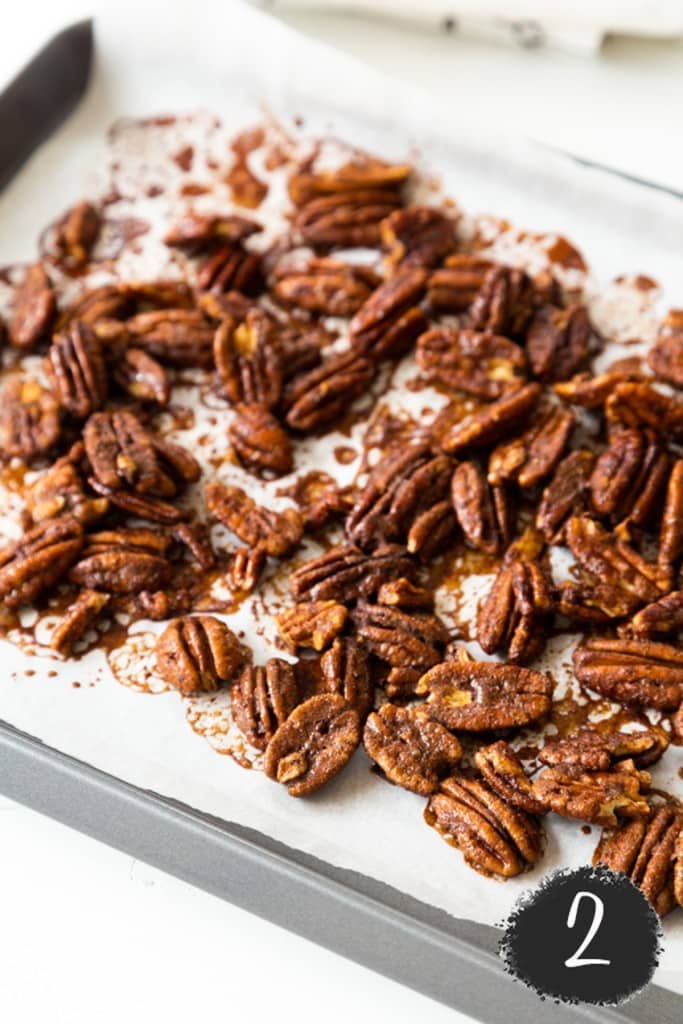 A parchment paper lined baking sheet with roasted cinnamon pecans.