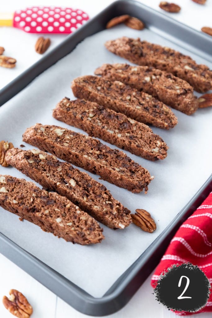 Chocolate biscotti cookies sliced and laid flat on a parchment lined baking sheet.