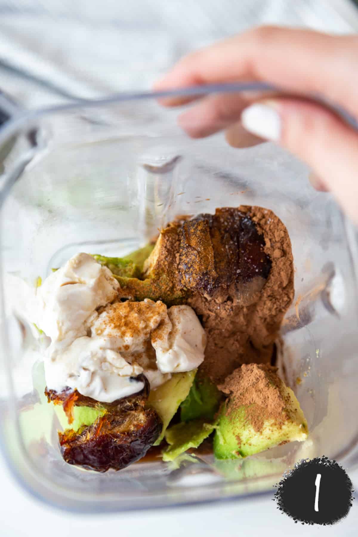 A blender with avocado, cocoa powder, dates, and cream.