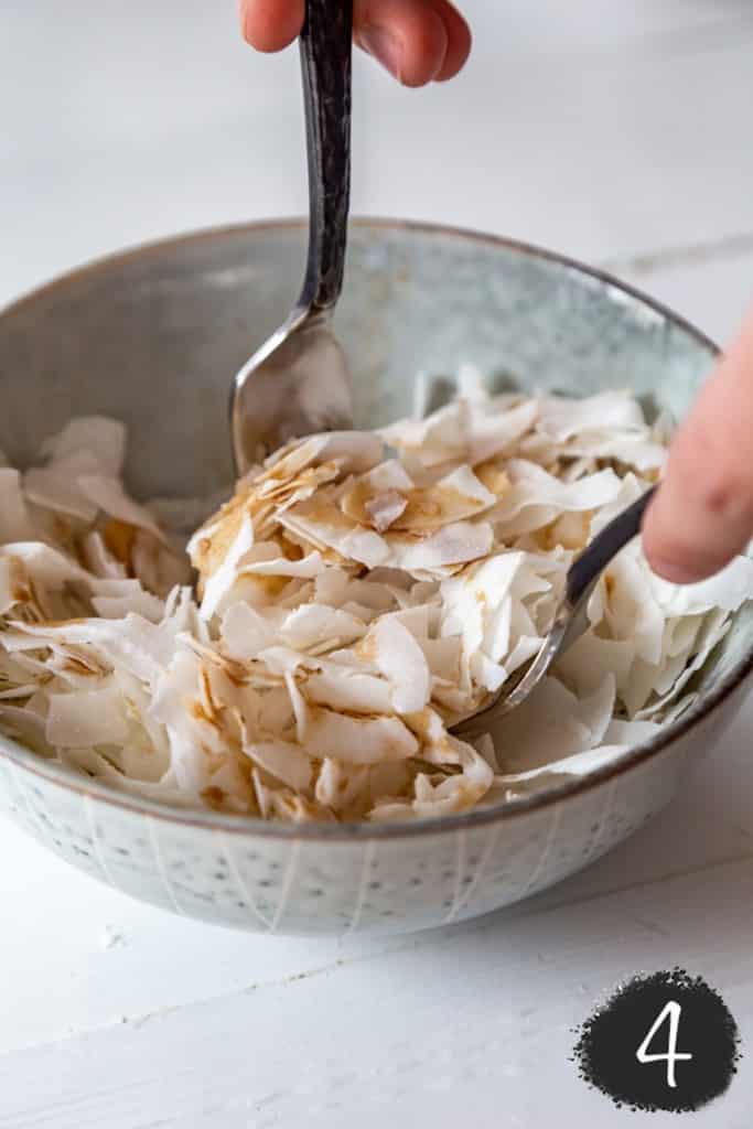 Two hands with forks tossing a brown liquid into coconut flakes.