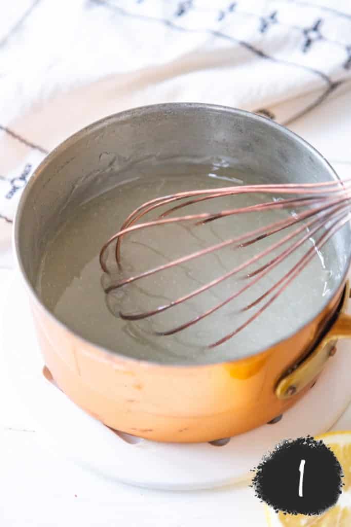 A copper pot with sugar and a whisk.
