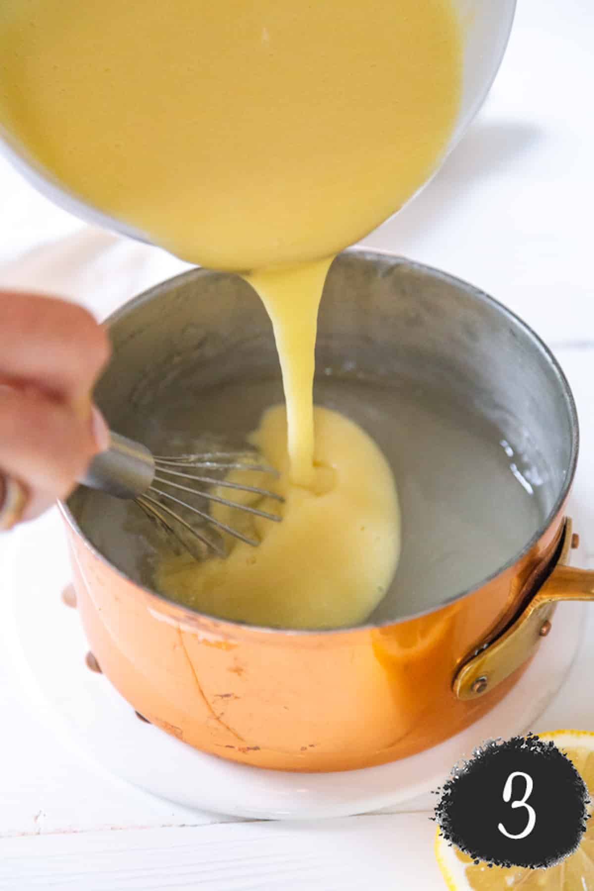 A bowl of egg mixture being poured into a copper pot and a hand is whisking the mixture.