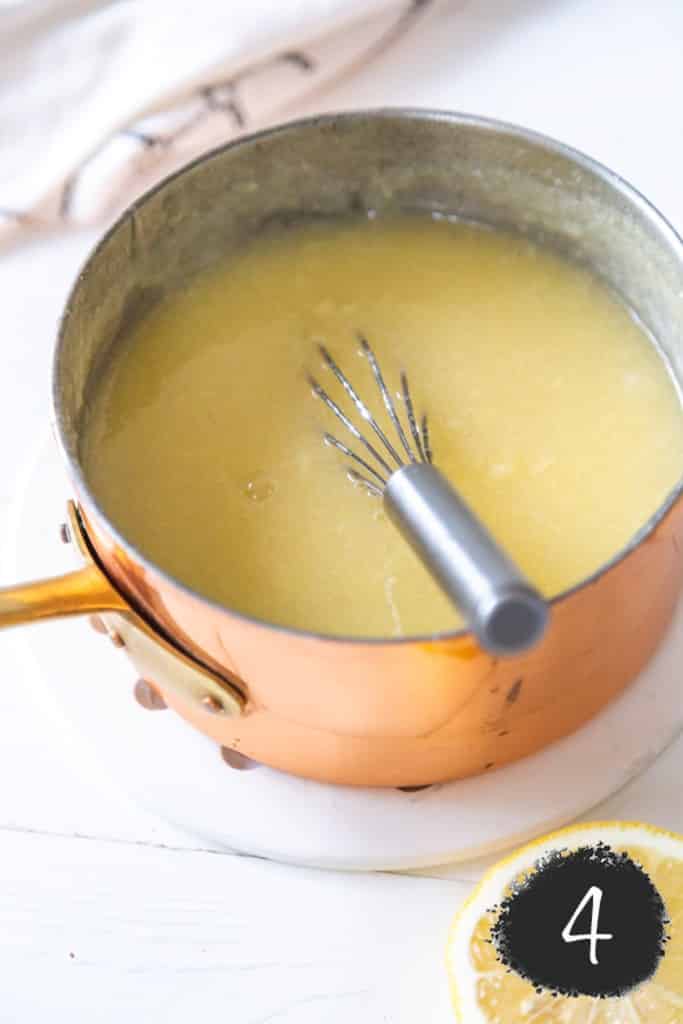 Lemon curd in a copper pot with a silver whisk.
