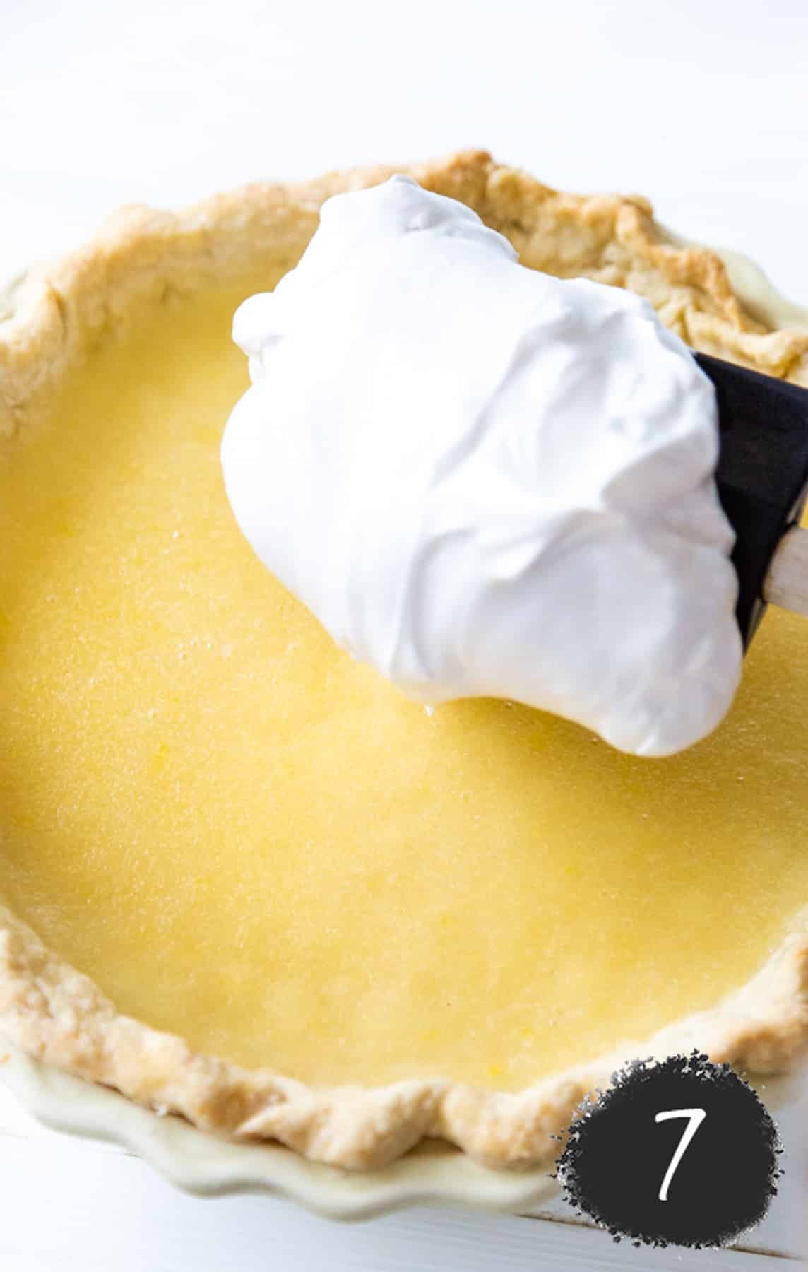 A lemon pie with a spoonful of meringue being placed on top of it.