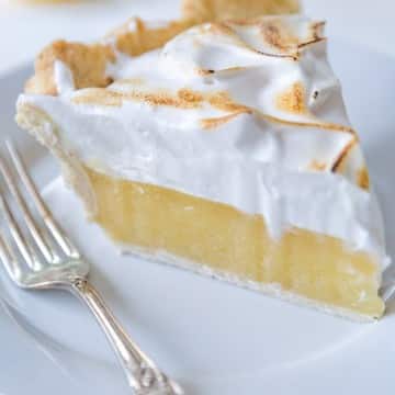 A slice of vegan lemon meringue pie on a white plate with a silver fork.