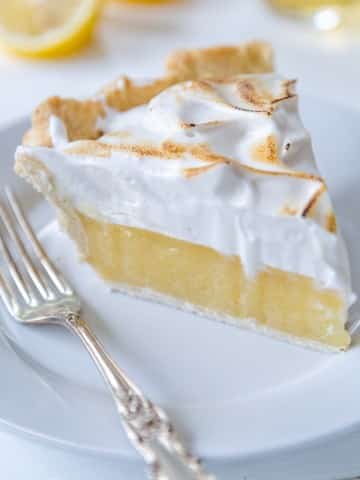 A slice of vegan lemon meringue pie on a white plate with a silver fork.