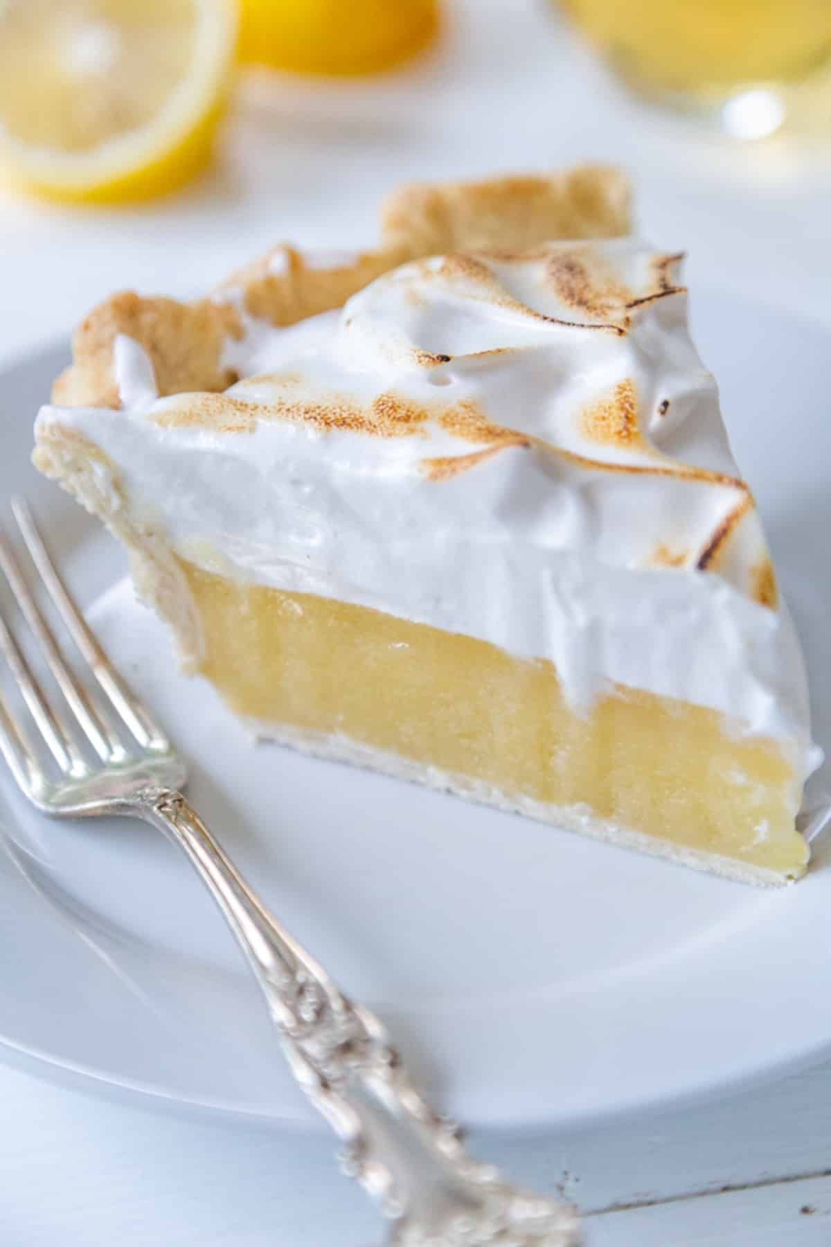 A slice of vegan lemon meringue pie on a white plate with a silver fork.